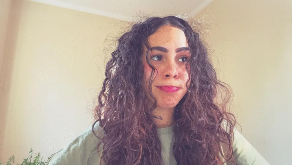 Mulher com cabelo cacheado sorrindo ao sol, mostrando fios definidos e sem frizz, simbolizando cuidado, hidratação e saúde capilar.